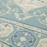 A close-up of a light blue and cream patterned rug with traditional medallion and floral motifs.
