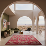A large red area rug with an ornate beige damask pattern is displayed in a modern, high-ceilinged desert-style living room with arched windows looking out onto a desert landscape.