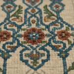 Close-up of a woven rug with an intricate floral and geometric pattern in blue, rust orange, olive green, and cream.