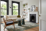 Modern living room with a white sofa, green rug, wooden armchair, and a fireplace.