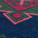 Close-up of a textured rug with a geometric pattern in navy blue, green, pink, and red.