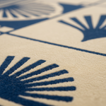 Close-up of a textured rug with a cream background and a bold navy blue geometric fan or scallop pattern.