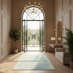 A large light green and blue abstract-patterned area rug lies on a herringbone wood floor in a grand, elegant interior hallway with beige walls, a chandelier, and an open arched doorway leading to a garden courtyard.