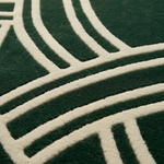 Close-up of a dark green textured rug with a raised cream-colored geometric pattern.