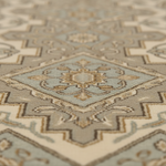 A close-up, shallow depth-of-field view of a traditional area rug featuring a geometric medallion pattern in beige, cream, light blue, and taupe.