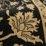 Close-up of a patterned rug with a black background and a large beige floral motif, showing the texture and detail of the pile.