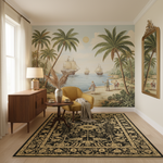 A styled interior room featuring a large vintage-style nautical mural with palm trees, sailing ships, and beach figures on the back wall. The room includes a mustard yellow armchair, a dark wood sideboard with a lamp, a round wooden coffee table with a vase, a patterned area rug, and a gold-framed mirror.