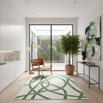 A modern living room interior with a large area rug featuring green abstract curved lines on a cream background. The room includes a brown leather armchair, a potted green tree, a black console table, and a large abstract painting on the wall.