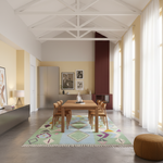 A modern dining room featuring a rectangular wooden dining table and six matching wooden chairs placed on a colorful geometric patterned area rug. The room has a high white-beamed ceiling, warm beige walls, sheer white curtains, and a dark red slatted accent wall in the background.