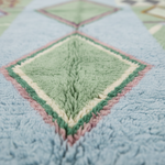 Close-up of a soft, textured rug with a geometric diamond pattern in pastel shades of light blue, mint green, cream, and dusty pink.