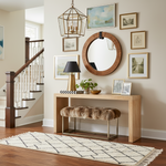 Foyer with wooden console table, round mirror, runner rug, and framed pictures on a beige wall.