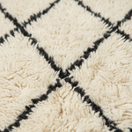 Close-up of a textured cream shag rug with a black geometric diamond pattern.