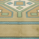 Close-up of a textured area rug with a geometric pattern in beige, light blue, sage green, and cream.