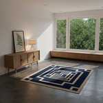 A modern living room with a navy blue and beige geometric area rug on dark gray tile flooring. A light wood credenza with a framed botanical print and a small table lamp sits on the left, and a built-in wooden window seat with large windows showing green foliage outside is on the right.