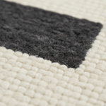 Close-up of a woven textile with a dark charcoal gray corner and cream-colored textured sections.