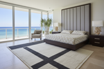 Modern bedroom with ocean view, large bed, knotted beige rug, and decorative elements.