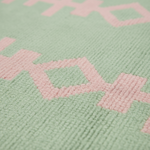 Close-up of a textured knit fabric with a geometric pattern in pale mint green and light pink.