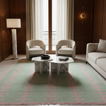 A styled living room interior featuring a large sage green area rug with a pink geometric cross pattern, two cream armchairs, a marble coffee table, a sofa, wood-paneled walls, and a floor lamp.