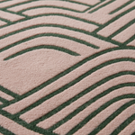 Close-up of a textured fabric or carpet with a repeating geometric wave-like pattern in dark green on a dusty pink background.