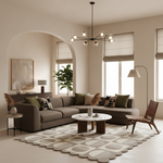A modern living room featuring a large taupe sectional sofa, a matching patterned area rug, a round coffee table, and a brown woven accent chair. The room has warm beige walls, large windows with beige roller shades, and a black multi-arm chandelier.