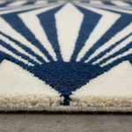 Close-up of a textured area rug with a navy blue and cream geometric fan pattern, shown on a concrete floor.