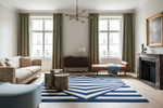 A styled living room interior featuring a prominent navy blue and cream geometric patterned area rug on a light wood floor. The room includes a beige sofa, olive green curtains, a brown leather chaise lounge, a dark wood sideboard, a fireplace with a marble mantel, and a modern brass chandelier.