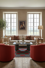 Living room with red rug, chairs, white sofa, and large windows.