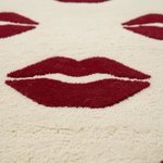 A close-up of a textured cream-colored rug featuring a repeating pattern of deep red lips.