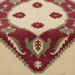 A close-up of a patterned rug with a cream background, deep burgundy floral motifs, and sage green geometric and leaf details.
