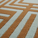 Close-up of a textured area rug with a geometric maze-like pattern in warm tan and pale icy blue.