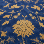 A close-up of a textured rug featuring a deep blue base with a raised mustard-gold floral and vine pattern.
