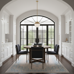 A modern dining room featuring a round wooden dining table with four black upholstered chairs, set on a blue patterned area rug. The room has white cabinetry on both sides, a large black-framed arched window in the back, and a gold pendant light hanging above.