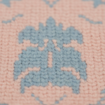 Close-up of a knitted textile with a light blue geometric pattern on a soft pink background.