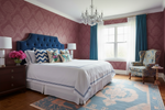 Luxurious bedroom with a blue upholstered bed, floral pillows, and a a persian rug.