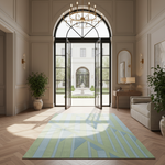 A large rectangular area rug with a geometric stripe pattern in shades of sage green, light blue, and cream is displayed in a grand, elegant foyer with herringbone wood floors and an open glass door leading to a courtyard.