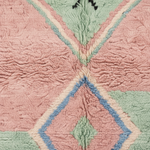 A close-up of a textured, sherpa-like rug featuring a geometric pattern in dusty pink, sage green, light blue, and cream.