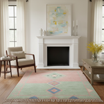 A rectangular area rug with a pink, sage green, and blue geometric diamond pattern and cream fringe, styled in a bright, modern living room in front of a white fireplace.
