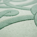 Close-up of a plush textured rug with a raised leaf or vine pattern in soft sage green and pale mint green.