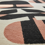 Close-up of a textured area rug with a modern geometric pattern in black, dusty rose, and cream.