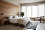 A modern bedroom interior with a low wooden bed frame, white bedding, a beige throw blanket, a dark gray patterned rug, a wood-paneled headboard wall, sheer curtains, a chair, and a potted plant.