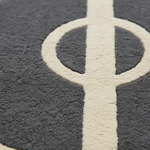 Close-up of a dark gray textured rug with a large cream-colored circular and vertical geometric pattern.