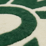 Close-up of a plush rug with a geometric pattern in dark green and off-white, showing the high-pile texture and curved lines of the design.