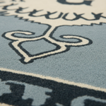 Close-up of a textured area rug with a light blue field, dark navy abstract border, and cream-colored stylized lettering and motifs.