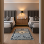 A rectangular area rug with a light blue-gray background and a central deer-themed crest, styled in a modern bedroom between two gray upholstered beds.
