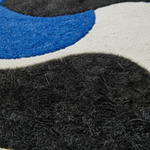 Close-up of a textured area rug with an abstract wavy pattern in black, blue, off-white, and gray.