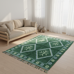 A green area rug with a geometric diamond pattern and tassels, styled on a light wood floor in a bright living room next to a beige sofa.
