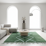 A green area rug with a white geometric diamond pattern and fringe, styled in a bright, modern living room with a light gray sectional sofa, a wooden coffee table, and a tall floor lamp.