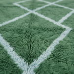 Close-up of a green plush fabric with a white geometric diamond pattern, showing soft texture and shallow depth of field.