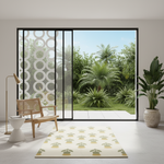 A rectangular cream rug with a repeating green potted plant pattern is styled in a modern minimalist room with a large glass sliding door overlooking a lush green garden.