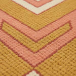 Close-up of a textured woven rug with a geometric chevron pattern in mustard yellow, dusty pink, terracotta red, and cream.